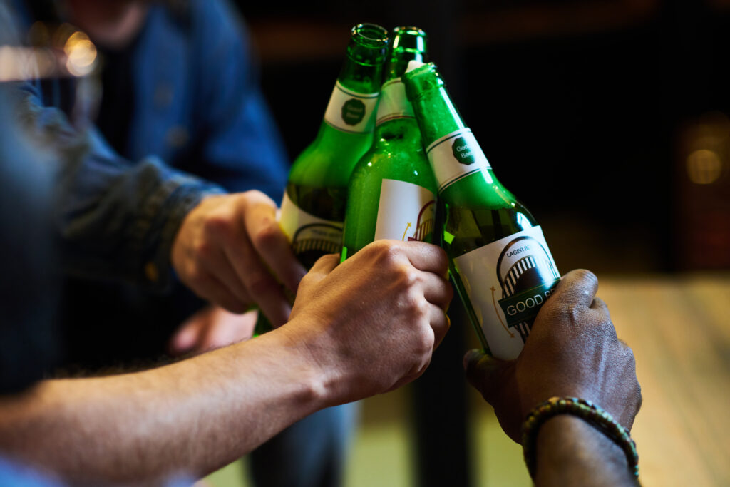 Hands of three young interracial men clinking with bottles of beer